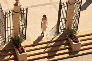 Une femme descend un escalier orné de part et d’autre de jardinières et d’une grille.