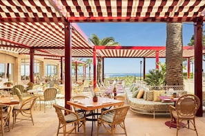 Een terras met rieten meubilair, uitzicht op de zee en een rood-wit gestreepte luifel.