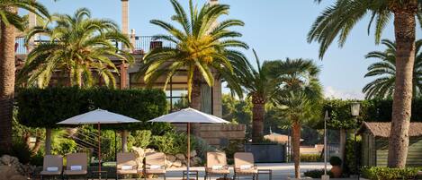 A pool area with lounge chairs and umbrellas, surrounded by palm trees and a building with a tower.