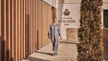 A person walking on a pathway beside a building with a sign that reads 'CASTILLO HOTEL SON VIDA SPA'.