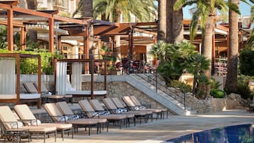 A poolside area with lounge chairs and a swimming pool, surrounded by palm trees and a building with balconies.