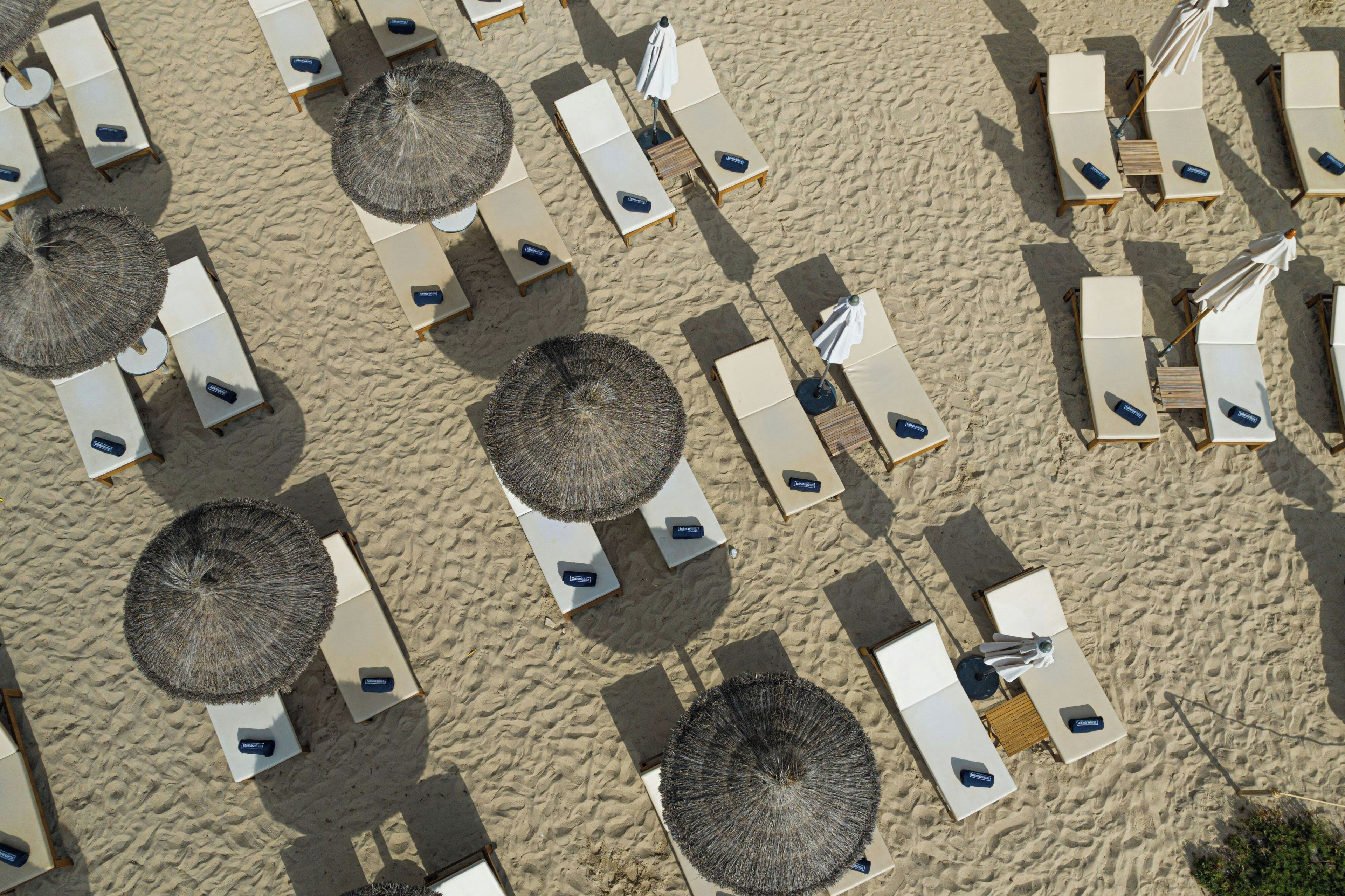 Vista aérea de una playa con filas de tumbonas y sombrillas de paja.