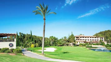 A golf course with a clubhouse, palm trees, and a large building in the background.