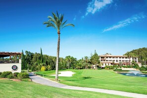 Ein Golfplatz mit Klubhaus, Palmen und einem großen Gebäude im Hintergrund.