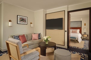 A hotel room with a sofa, armchair, coffee table, and a TV on the wall.