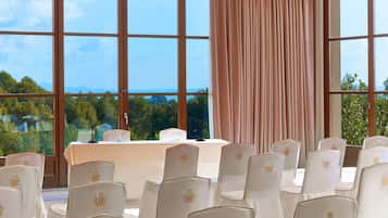 A conference room with a table and chairs, large windows with a view of greenery and mountains, and a curtain on one side.