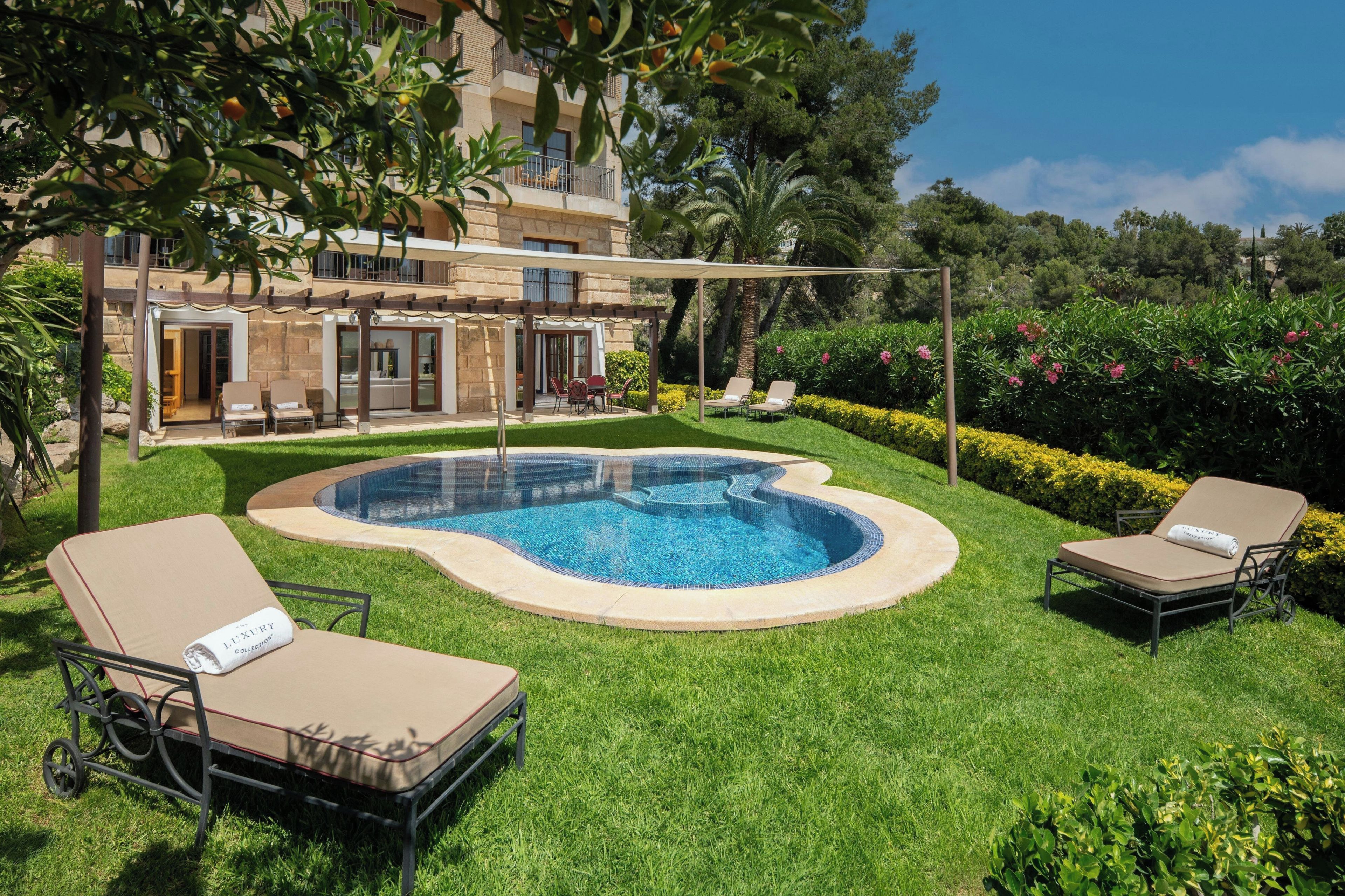 A swimming pool with lounge chairs, a pergola, and a building in the background.