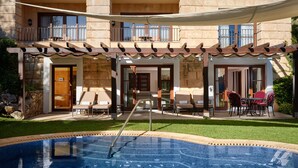 Un espace piscine doté d’un jacuzzi, de coins salon extérieurs et d’un bâtiment en pierre avec des balcons.