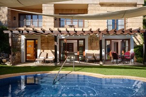 Un área de piscina con jacuzzi, mobiliario exterior y un edificio de piedra con balcones.