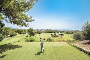 Een golfbaan met vrij uitzicht over het landschap, inclusief bomen en verre gebouwen.
