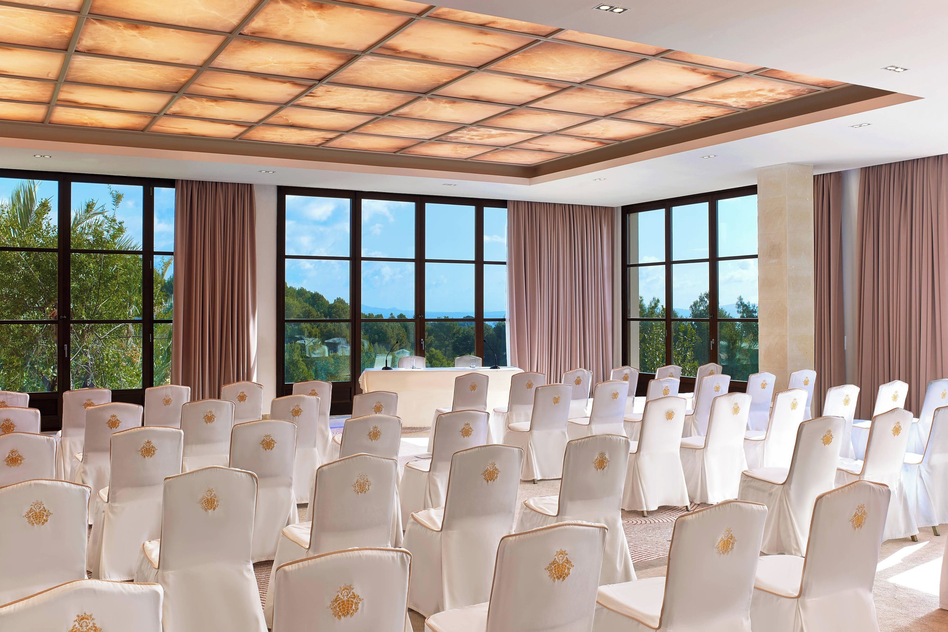 A conference room with rows of white chairs, large windows, and a ceiling with a grid pattern.
