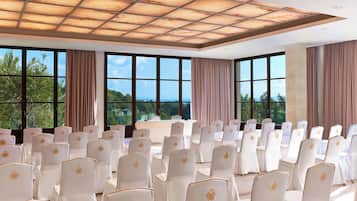 A conference room with rows of white chairs, large windows, and a ceiling with a grid pattern.
