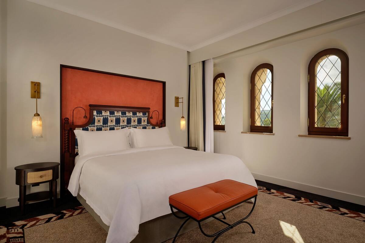 Une chambre à coucher bien aménagée, avec un grand lit, une table de chevet, une lampe de lecture et une fenêtre donnant sur un beau paysage.