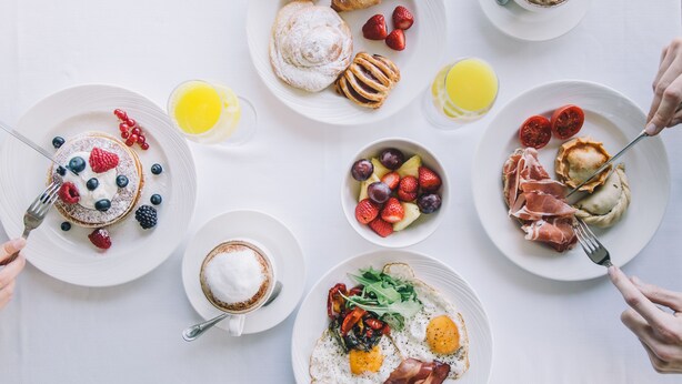 Une table dressée pour le petit-déjeuner, avec divers plats, notamment des viennoiseries, des fruits et des œufs.