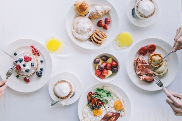 Une table dressée pour le petit-déjeuner, avec divers plats, notamment des viennoiseries, des fruits et des œufs.