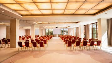 A conference room with rows of red chairs, a large screen at the front, and a ceiling with a grid pattern.