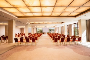 A conference room with rows of red chairs, a large screen at the front, and a ceiling with a grid pattern.