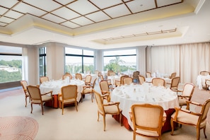 A large conference room with round tables and chairs, large windows with a view of greenery, and a modern ceiling design.