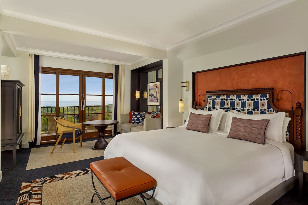 Une chambre d’hôtel avec un grand lit, un bureau, une chaise, un balcon avec vue et une tête de lit en bois.