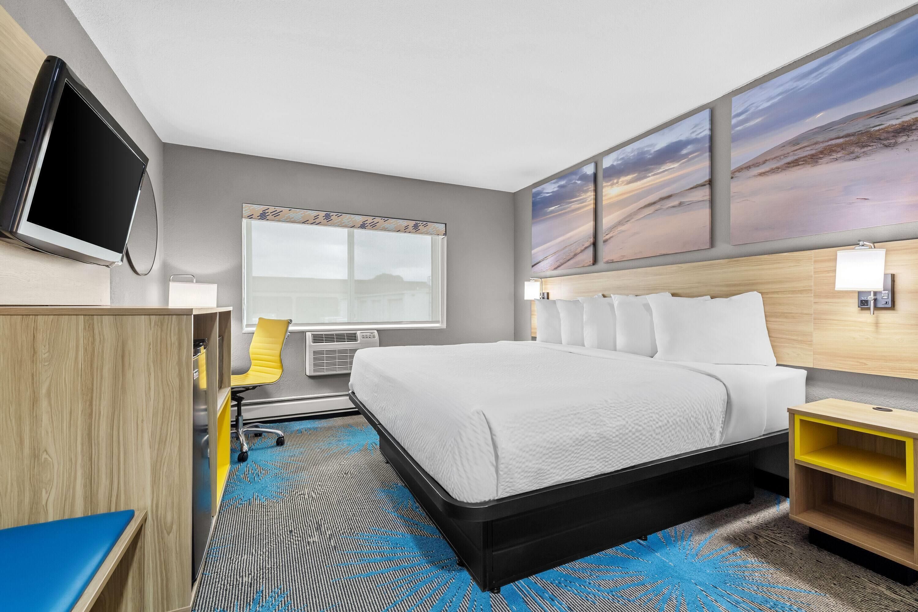 Una habitación de hotel con cama, escritorio, silla, televisión y obras de arte en la pared.