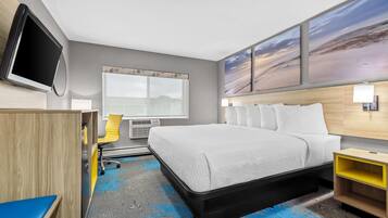 A hotel room with a bed, a desk, a chair, a television, and artwork on the wall.