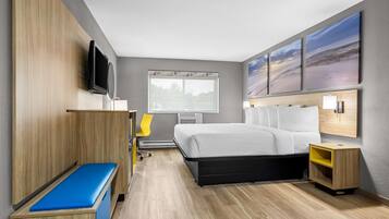 Une chambre d’hôtel moderne équipée d’un lit, d’une banquette, d’une télévision, d’un bureau et d’œuvres d’art accrochées au mur.