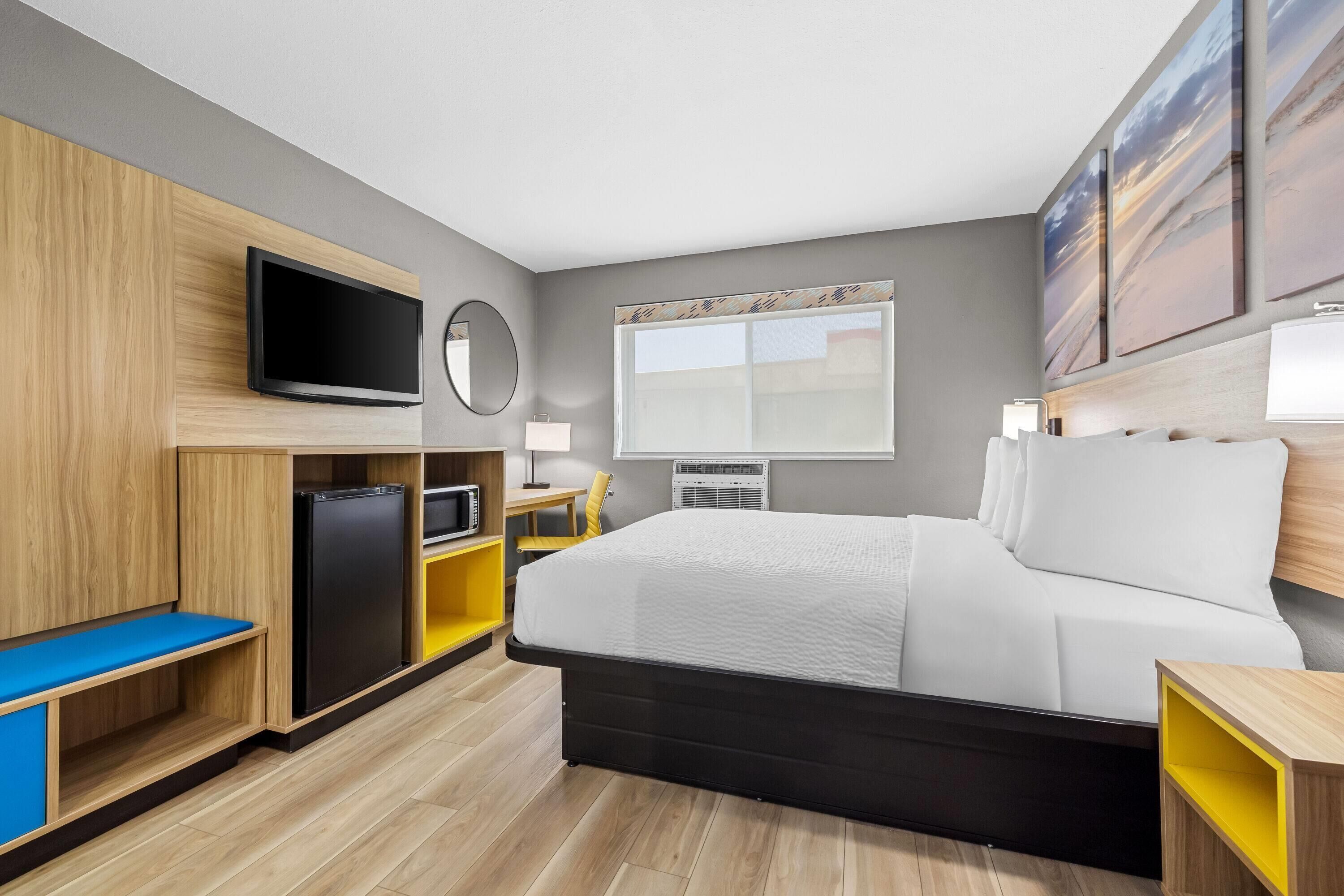 A hotel room with a bed, a TV, a desk with a chair, a small refrigerator, and a window with a view.