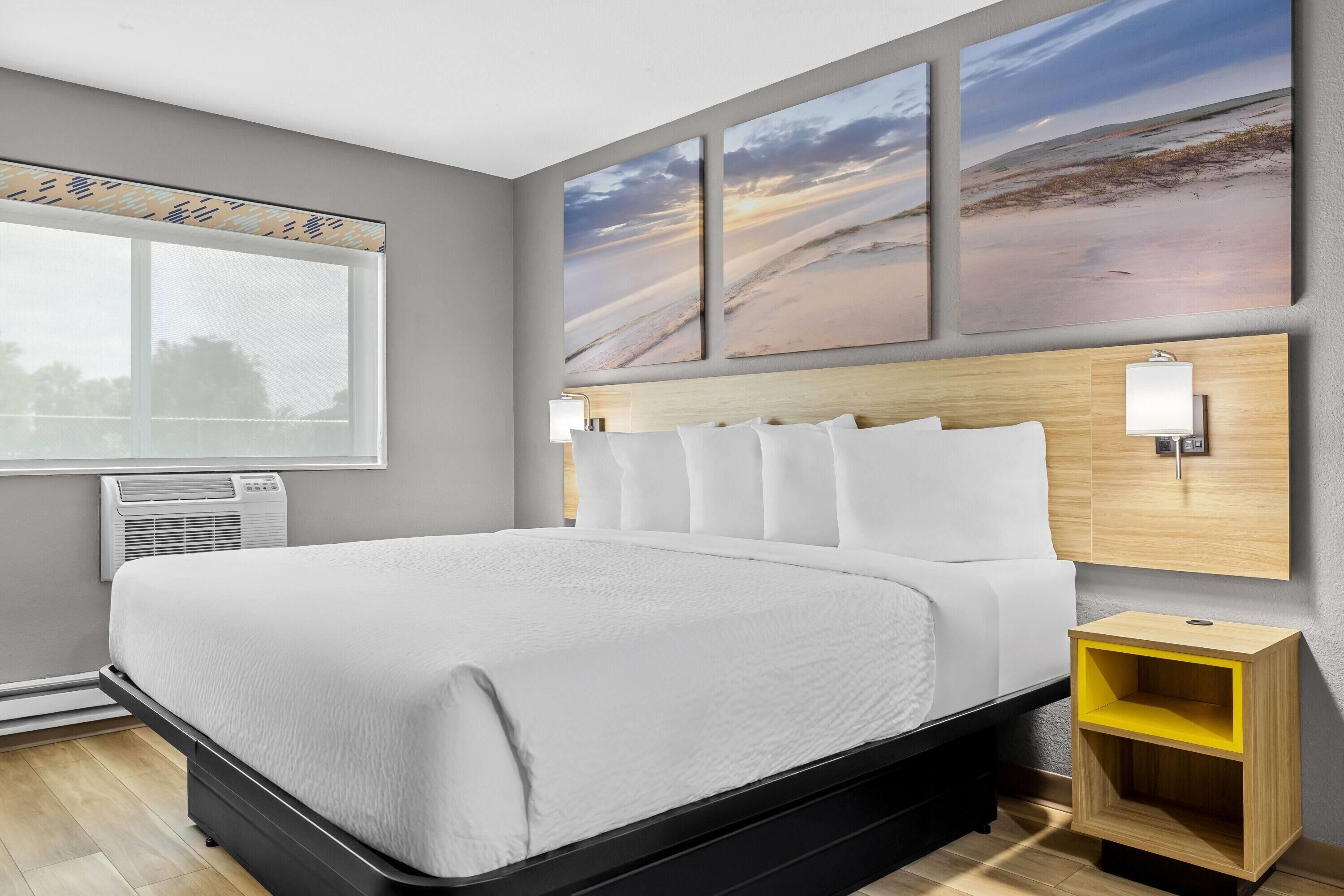 Une chambre d’hôtel moderne avec un grand lit, une fenêtre et trois œuvres d’art accrochées au mur.