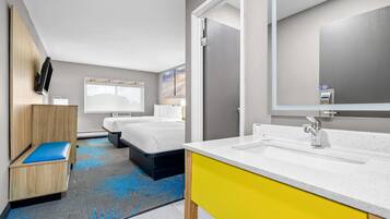 A hotel room with a bed, a small seating area, a bathroom with a sink and mirror, and a large window.