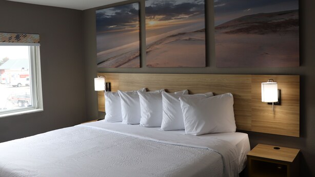 A hotel room with a large bed, two wall-mounted lamps, a nightstand, and three landscape paintings on the wall. - Days Inn by Wyndham La Crosse (La Crosse)