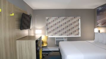 A hotel room with a bed, a desk, a chair, a TV, and a window with patterned curtains.