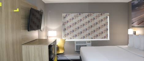 Habitación de hotel con cama, escritorio, silla, televisor y ventana con cortinas estampadas.