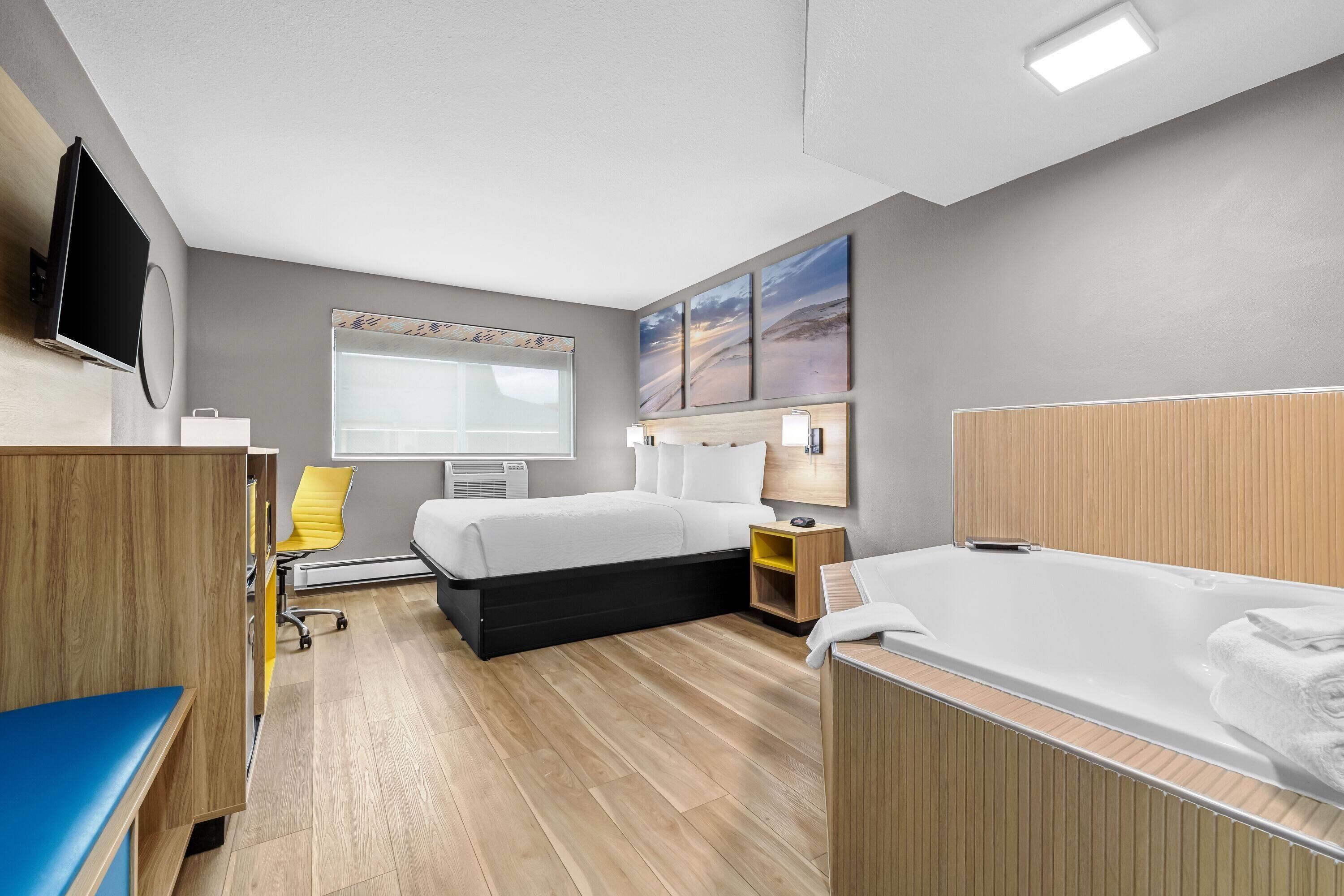 Una habitación de hotel moderna con cama, mesita de noche, lámpara, televisor y ventana.