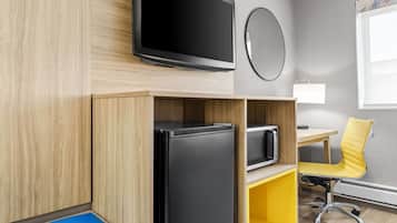 A modern room with a flat-screen TV, a refrigerator, a microwave, a yellow office chair, and a desk.