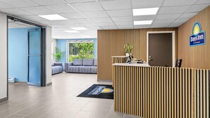 A reception area with a Days Inn sign, a reception desk, a blue wall, a grey sofa, and a plant. - Days Inn by Wyndham La Crosse (La Crosse)
