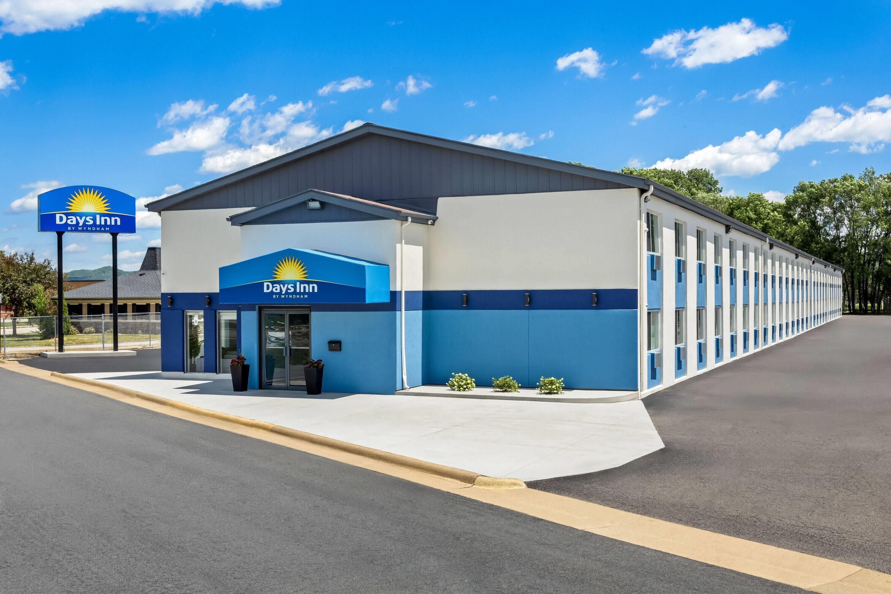 A Days Inn by Wyndham with a single-story structure, a parking lot, and a clear sky.