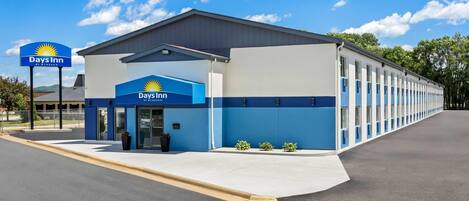A Days Inn by Wyndham with a single-story structure, a parking lot, and a clear sky.