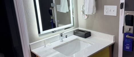 Een badkamer met een spiegel, twee wastafels, een handdoekhouder en een deur met een handgreep.