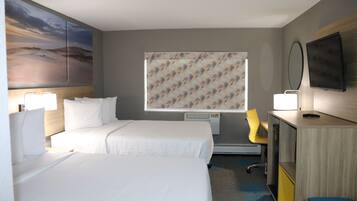Quarto de hotel com duas camas, uma escrivaninha, uma cadeira, uma televisão e uma janela com cortina estampada.