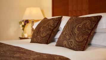 A neatly made bed with two patterned pillows, a bedside lamp, and a vase with flowers.