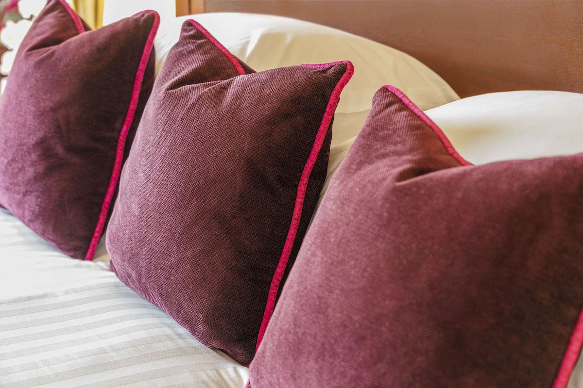 A bed with striped bedding and four pillows with a red trim.