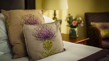 Una cama con dos almohadones decorativos con diseño floral, una mesita de noche con un florero y una lámpara.