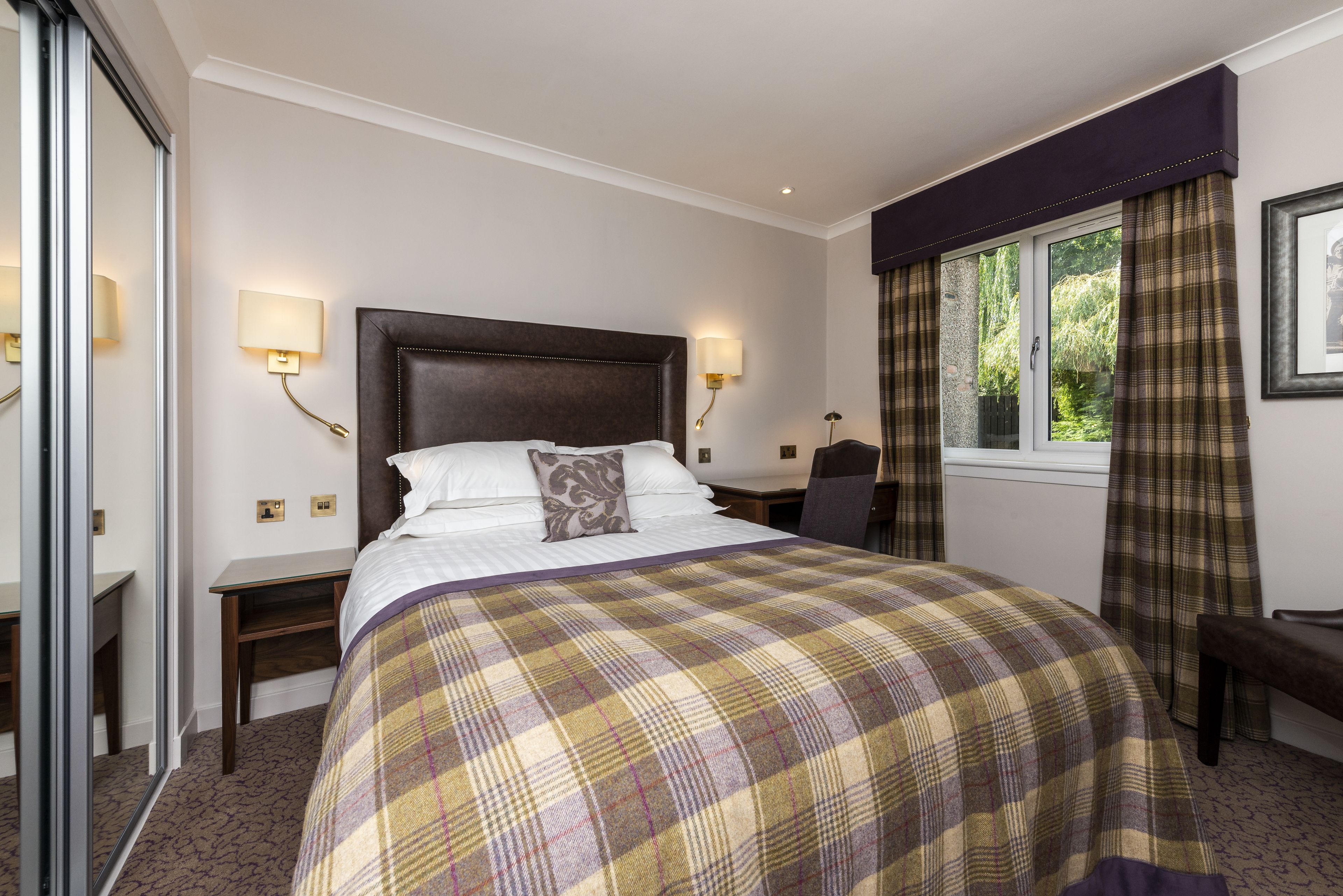 A hotel room with a large bed, two bedside tables, a chair, a desk, and a window with curtains.