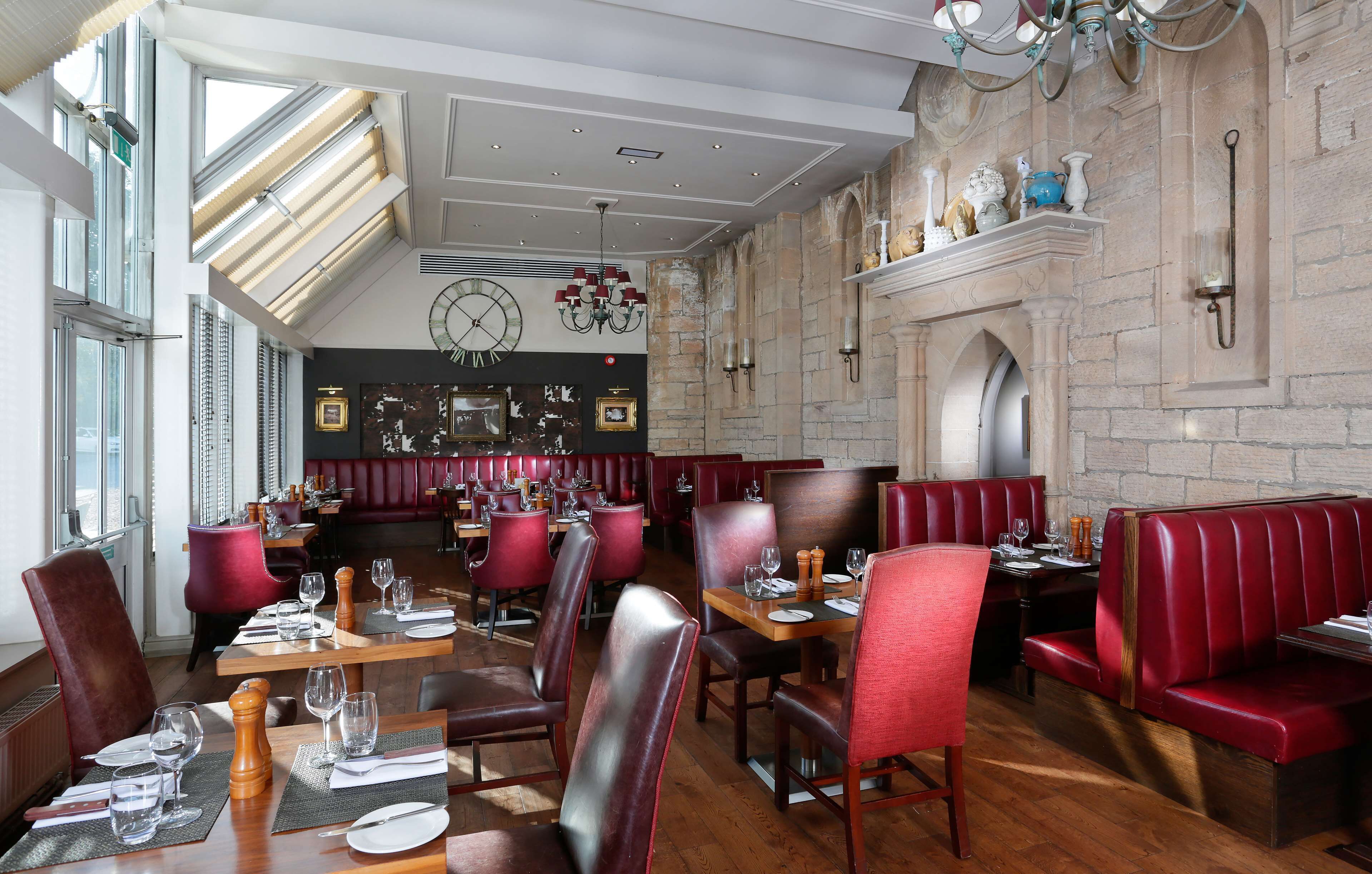 A restaurant with red leather booths and tables, wooden floors, and a stone wall.
