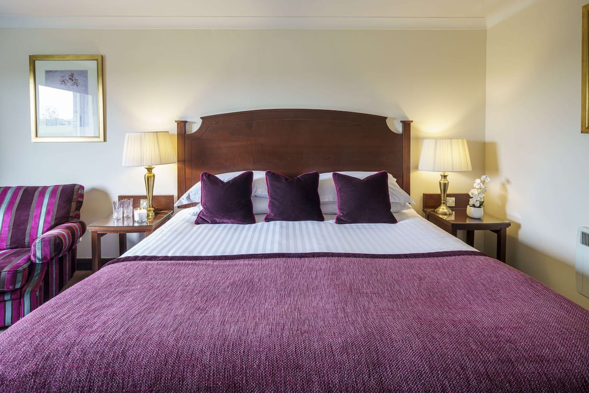 A hotel room with a large bed, two bedside tables with lamps, a striped armchair, and a framed picture on the wall.