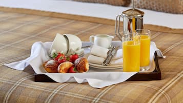Bandeja de desayuno con cruasanes, fresas, una cafetera, tazas y vasos de jugo de naranja sobre un mantel a cuadros.