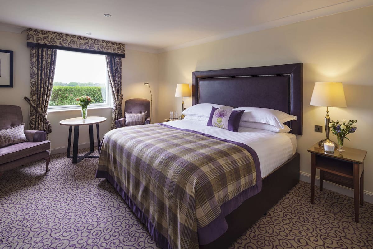 A hotel room with a large bed, a small round table, a chair, and a sofa.