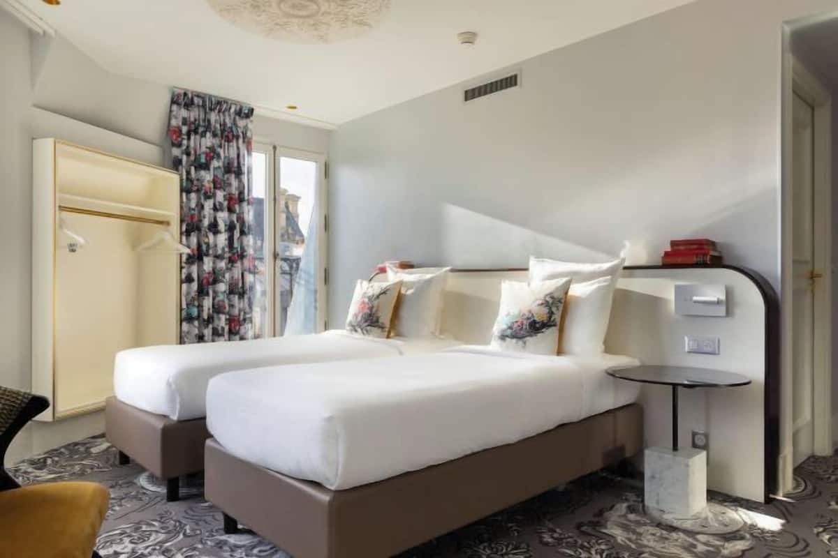 A hotel room with two beds, a small table, a chair, and a wardrobe.