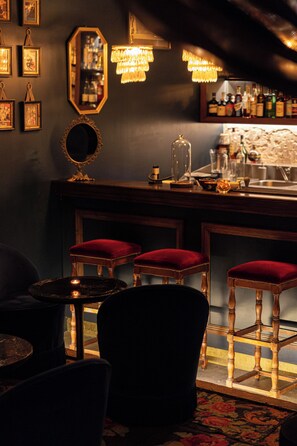 A bar area with wooden stools, a mirror, and a chandelier.