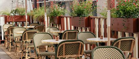 Outdoor seating with wicker chairs and tables, surrounded by planters with flowers.